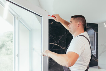 The worker adjusts the window in the apartment of the house after repair