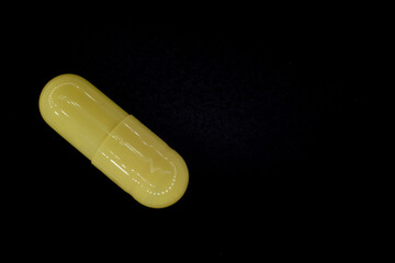 yellow pill in a capsule on a black, rough background, macro photo