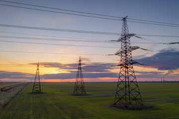 high voltage lines and power pylons in a green agricultural field against a saturated sunset sky