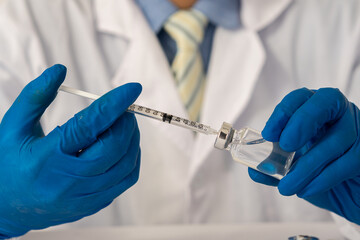 Male doctor's hand wearing blue medical gloves holding a syringe injecting coronavirus covid 19 vaccine from a pre-injection vial. vaccination concept to prevent influenza