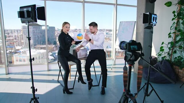 Creative people discussing business ideas showing design project in office. Young businessman and woman standing at desk and talking in front of professional cameras in light studio.