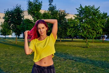 beautiful young girl with dyed pink hair, yellow crop top in city park