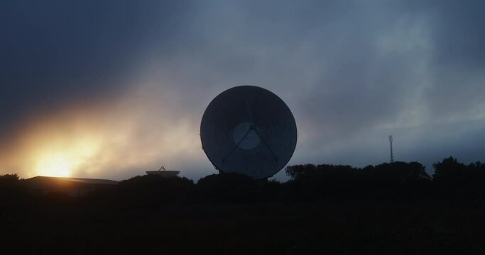 Dramatic sunset clouds and the sun behind a silhouette space antenna - zoom view