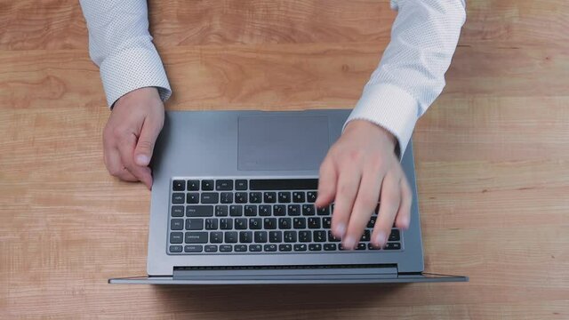 Man opening laptop and start working at home office, typing on keyboard on wooden work desk, top view
