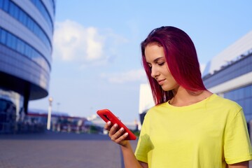 beautiful girl with dyed colored pink hair and bright clothes looks at phone