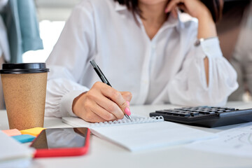 Cropped woman, close-up female hands holding pen making notes working in office, business concept. table desk, woman working, using smartphone, calculator. copy space