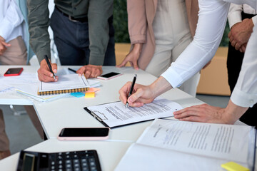 Signing contract, business agreement, deal concept. Business people signing official contract, formal document with pen on desk in modern bright office in the presence of colleagues co-workers