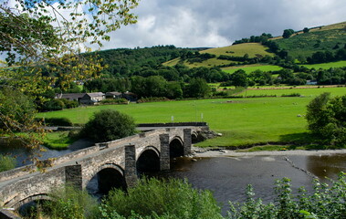 Fototapeta na wymiar Old stone bridge over the river Dee, near Llangollen, north Wales. Landscape aspect view. Rural scene with Green fields and wooded hills.