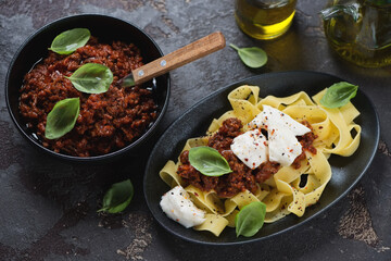 Pappardelle served with bolognese sauce, mozzarella cheese and green basil, studio shot on a brown stone background