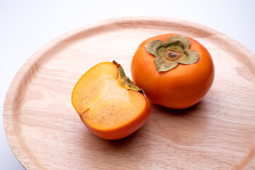 Video of slowly turning a persimmon on a wooden plate with a white background.