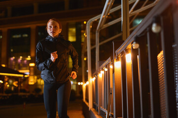 Attractive Slim Fitness Woman in Black Athletic Wear is Jogging In Night City Street. Female is Doing Workout at Night Alone,Young Redhead Lady Enjoy Being Healthy And Sporty, Preparing For Marathon