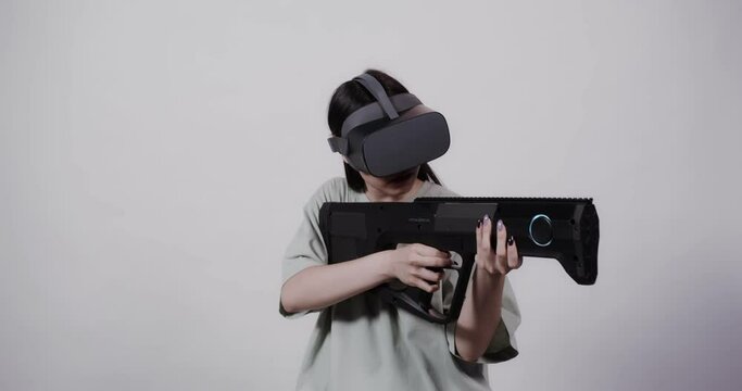Asian girl in virtual reality glasses with toy weapon plays in a 5D attraction