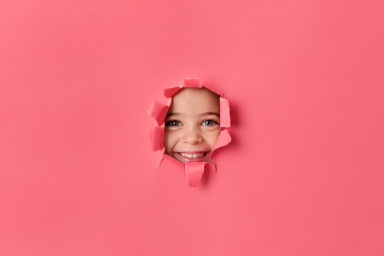 Happy little girl's face peeking through pink paper