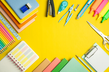 Stationery concept. Fat lay top view of notebook, clip board, color notepad, memo, dividers, colorful pencils, paper clips, dairy on yellow  background with copy space.