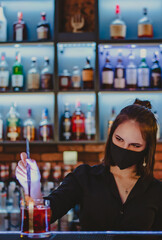 Portrait of young attractive woman bartender with mask Making Cocktail in bar
