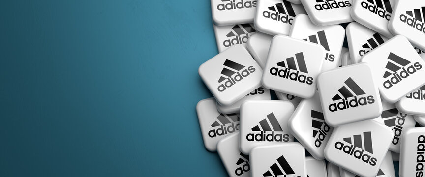 Logos of the German sportswear and apparel company Adidas AG. on a heap on a table. Copy space. Web banner format.