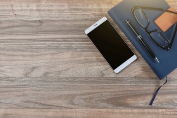 Cellphone, pen, and eyeglasses on the notebook on the wooden table 