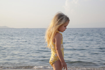 Adorable toddler girl in yellow swimsuit enjoying a day at the beach. Idyllic summer vacation.