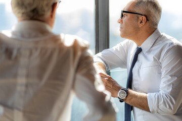 Picture of young business man talking to his older business partner. They are in white shirt and black tie. They are in a hotel lobby. 