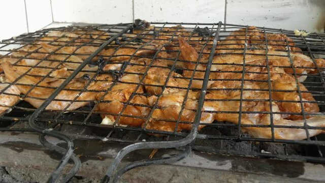 The grill grates and cooks chicken wings over hot coals. A fragrant smoke rises above them.