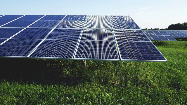 sunlight reflection close up on solar energy photovoltaic PV panels installed above the grass with nature background.