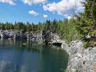 View of the rocks, the grotto and the emerald water of the Marble Canyon in the Ruskeala Mountain Park, which reflects the sky and clouds on a sunny summer day.