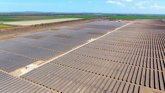 drone aerial view of vast solar energy farm with agriculture fields in countryside background.