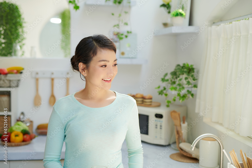 Wall mural Young beautiful modern woman stands near table on kitchen at home.