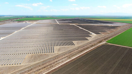 drone aerial view of vast solar energy farm with plowed agriculture fields in the countryside.