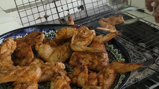 Complete dish with cooked barbecue wings. Transfer the cooked chicken wings to the plate from the grill grate. Close-up.
