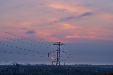 Beautiful early morning view of power lines with electricity transmission pylon and epic purple sunrise over Irish Sea seen from Ticknock Forest National Park, County Dublin, Ireland. Selective focus