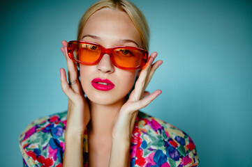 Fashionable  woman wearing trendy oval orange sunglasses, posing on blue background. Close up fashion portrait. Copy, empty space for text