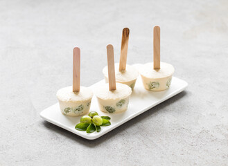 Children mini banana ice cream with gooseberries on a wooden stick on a ceramic plate on a light background