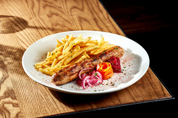 Grilled sausages with fries in a white plate on a wooden table. Currywurst