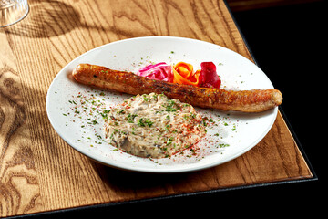 Grilled sausages with mushroom puree in a white plate on a wooden table. Currywurst