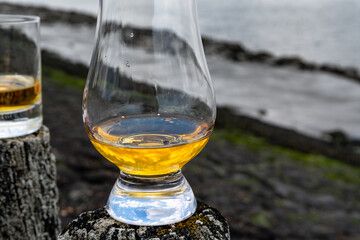 Tasting of dram single malt scotch whisky on seashore in Scotland, old wooden pole with whisky glass