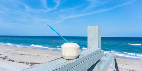 Peeled coconut with a straw on the railing of a wooden staircase as a symbol of a pleasant relaxation overlooking the ocean beach