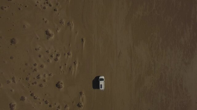 Vista aérea cenital con dron de una camper van circulando por una playa de arena en solitario