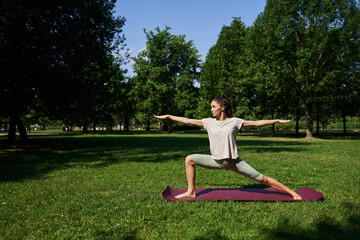 a girl in the park doing yoga and standing in the pose of the warrior VIRABHADRASAN I (Pose of the warrior Virabhadra)