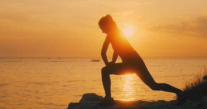 Young women are exercising in summer sunset with sea background. Warm-up, healthy running and outdoor exercise.