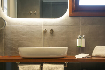 Modern simple bathroom with white bathroom sink standing on wooden shelf and backlit mirror