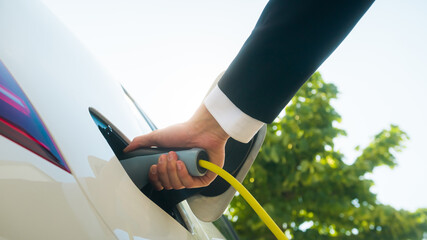 Male hands opening an electric car charging socket cap and plugging in a charger