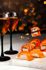 Sushi roll on a festive New Year's table on a marble board. There are two glasses of wine on the left. Beautiful bokeh on the background.