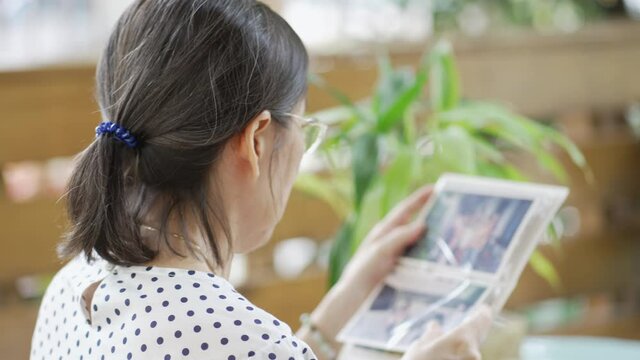 senior asian retired woman looking at old photo album at home terrace