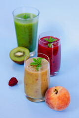 Top view of three different fresh delicious smoothies in a glasses made of peach, banana and berries with mint. Creative concept of healthy detox drink, diet or vegetarian food concept. Copy space.