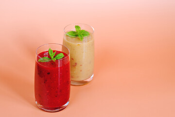 Top view of two different fresh healthy smoothies in a glasses made of peach, banana and berries with mint. Creative concept of healthy detox drink, diet or vegetarian food concept. Copy space.