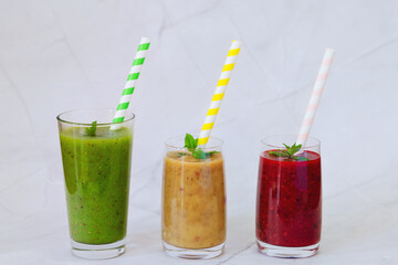 Top view of three different fresh delicious smoothies in a glasses made of peach, banana and berries with mint. Creative concept of healthy detox drink, diet or vegetarian food concept. Copy space.