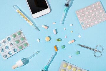 Tablets, pills, scissors, pipette, plastic medical disposable syringes, clinical manual thermometer and white phone  on pastel blue background. Minimal creative medical equipment concept. 