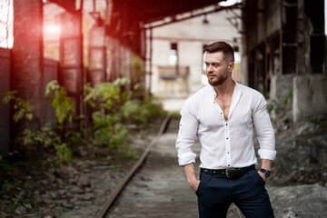 Handsome young male looking away while posing on broken building background. Stylish man in white...
