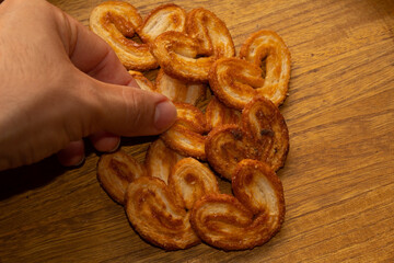a hand taking delicious freshly baked puff pastry ears on a wood colored board